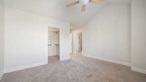 Unfurnished bedroom with lofted ceiling, a walk in closet, ceiling fan, light carpet, and a closet