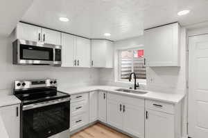 Kitchen featuring sink, white cabinetry, stainless steel appliances, a textured ceiling, and light wood-type flooring