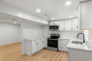 Kitchen with sink, white cabinetry, stainless steel appliances, light stone counters, and light wood-type flooring