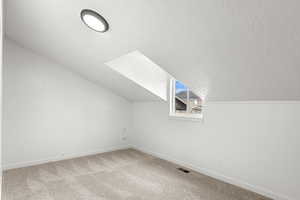 Bonus room featuring carpet flooring, a textured ceiling, and lofted ceiling with skylight