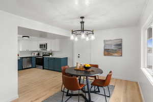 Dining space with crown molding, a textured ceiling, an inviting chandelier, and light hardwood / wood-style flooring