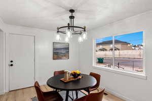 Dining area with ornamental molding, a notable chandelier, a textured ceiling, and light hardwood / wood-style flooring