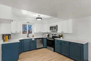 Kitchen featuring blue cabinets, sink, light wood-type flooring, appliances with stainless steel finishes, and white cabinets