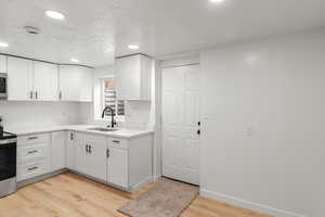 Kitchen with white cabinetry, sink, stainless steel electric stove, and light hardwood / wood-style flooring