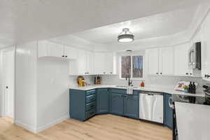 Kitchen featuring blue cabinets, sink, white cabinets, stainless steel appliances, and light hardwood / wood-style flooring