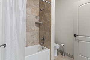 Bathroom with tile patterned flooring, shower / bathtub combination with curtain, and toilet