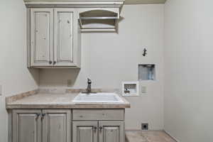 Clothes washing area with cabinets, hookup for a washing machine, sink, and hookup for an electric dryer