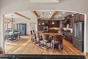 Kitchen featuring a spacious island, decorative light fixtures, dark brown cabinets, high quality appliances, and custom range hood