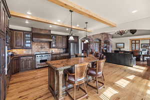 Kitchen with dark brown cabinets, appliances with stainless steel finishes, a kitchen breakfast bar, custom range hood, and backsplash