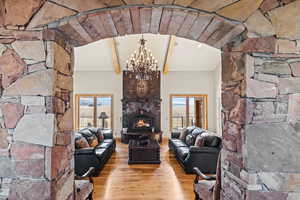 Unfurnished living room with beam ceiling, a stone fireplace, an inviting chandelier, and light wood-type flooring