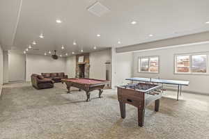 Recreation room with light colored carpet, a stone fireplace, and billiards