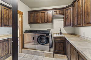 Washroom featuring sink, light tile patterned floors, washer and clothes dryer, and cabinets