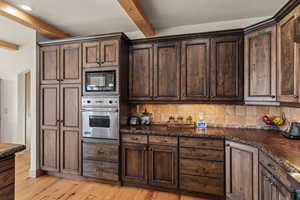 Kitchen featuring black microwave, backsplash, oven, beam ceiling, and light hardwood / wood-style flooring