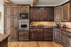 Kitchen with backsplash, black microwave, dark brown cabinetry, oven, and beamed ceiling