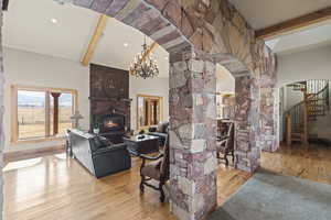 Living room featuring an inviting chandelier, light hardwood / wood-style flooring, a large fireplace, and beamed ceiling