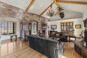 Living room with lofted ceiling with beams, a notable chandelier, light wood-type flooring, and a fireplace