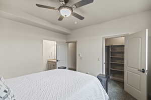 Bedroom with a walk in closet, ensuite bath, dark carpet, a closet, and ceiling fan