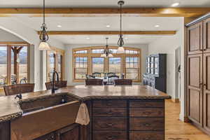 Kitchen with lofted ceiling, sink, hanging light fixtures, dark brown cabinetry, and light hardwood / wood-style floors