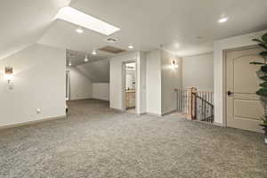 Bonus room with vaulted ceiling with skylight and light carpet