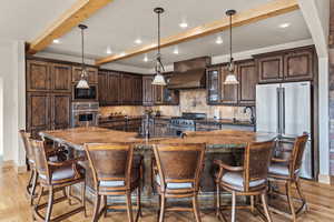 Kitchen featuring custom exhaust hood, pendant lighting, premium appliances, and a spacious island