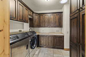 Clothes washing area featuring light tile patterned floors, washing machine and dryer, and cabinets