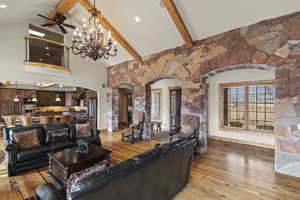 Living room featuring beamed ceiling, high vaulted ceiling, ceiling fan with notable chandelier, and light wood-type flooring