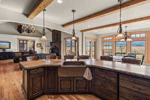 Kitchen with lofted ceiling with beams, hanging light fixtures, sink, and dark brown cabinets