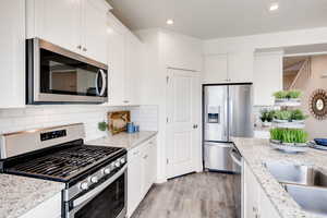 Kitchen with white cabinetry, appliances with stainless steel finishes, light stone counters, and backsplash