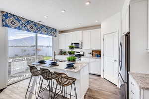 Kitchen featuring sink, a center island with sink, appliances with stainless steel finishes, light stone countertops, and white cabinets