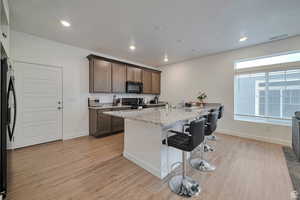 Kitchen with light stone countertops, black appliances, a breakfast bar, and light wood-type flooring