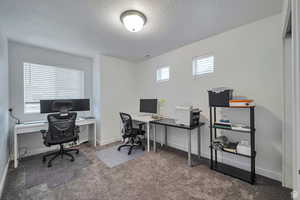 Office space with a textured ceiling and dark colored carpet