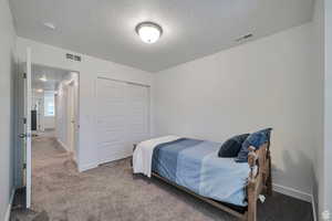 Bedroom featuring light carpet, a textured ceiling, and a closet