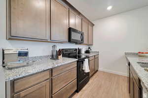 Kitchen featuring light stone countertops, a textured ceiling, light wood-type flooring, and black appliances