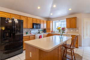 Kitchen with a kitchen bar, a center island, light tile floors and vaulted ceilings