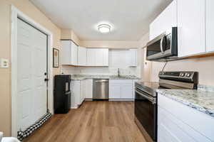 Kitchen featuring sink, light stone counters, appliances with stainless steel finishes, hardwood / wood-style floors, and white cabinets