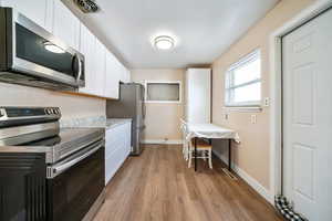 Kitchen with white cabinetry, appliances with stainless steel finishes, and light wood-type flooring