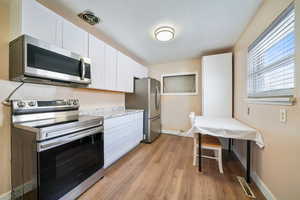 Kitchen featuring light hardwood / wood-style flooring, light stone countertops, white cabinets, and appliances with stainless steel finishes