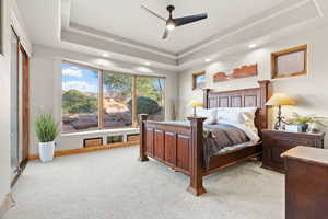 Carpeted bedroom with a raised ceiling and ceiling fan