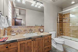 Full bathroom with tile patterned floors, toilet, combined bath / shower with glass door, vanity, and decorative backsplash