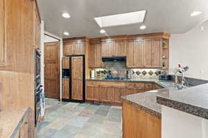 Kitchen with kitchen peninsula, a skylight, sink, backsplash, and black appliances