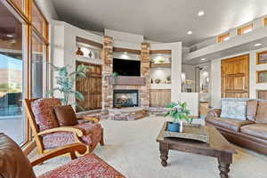 Carpeted living room with a stone fireplace and built in shelves