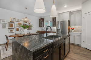 Kitchen featuring sink, decorative light fixtures, dark stone counters, stainless steel appliances, and a kitchen island with sink