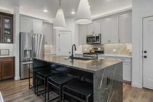 Kitchen featuring a breakfast bar area, a kitchen island with sink, dark stone countertops, stainless steel appliances, and dark hardwood / wood-style flooring