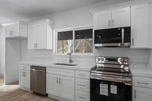 Kitchen with appliances with stainless steel finishes, sink, and white cabinets