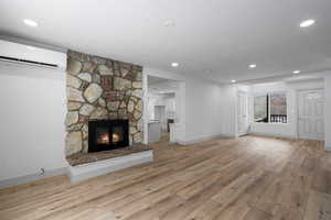 Unfurnished living room with a stone fireplace, a wall mounted air conditioner, and light hardwood / wood-style floors