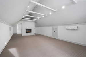 Unfurnished living room featuring lofted ceiling with beams, a wall unit AC, and carpet