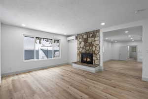 Unfurnished living room featuring a stone fireplace, light wood-type flooring, a textured ceiling, and an AC wall unit