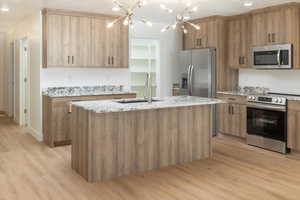 Kitchen featuring sink, light stone counters, light wood-type flooring, appliances with stainless steel finishes, and a kitchen island with sink