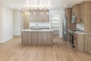 Kitchen featuring sink, an island with sink, pendant lighting, stainless steel appliances, and light stone countertops