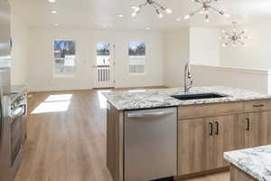 Kitchen featuring dishwasher, sink, a kitchen island with sink, a notable chandelier, and light hardwood / wood-style floors